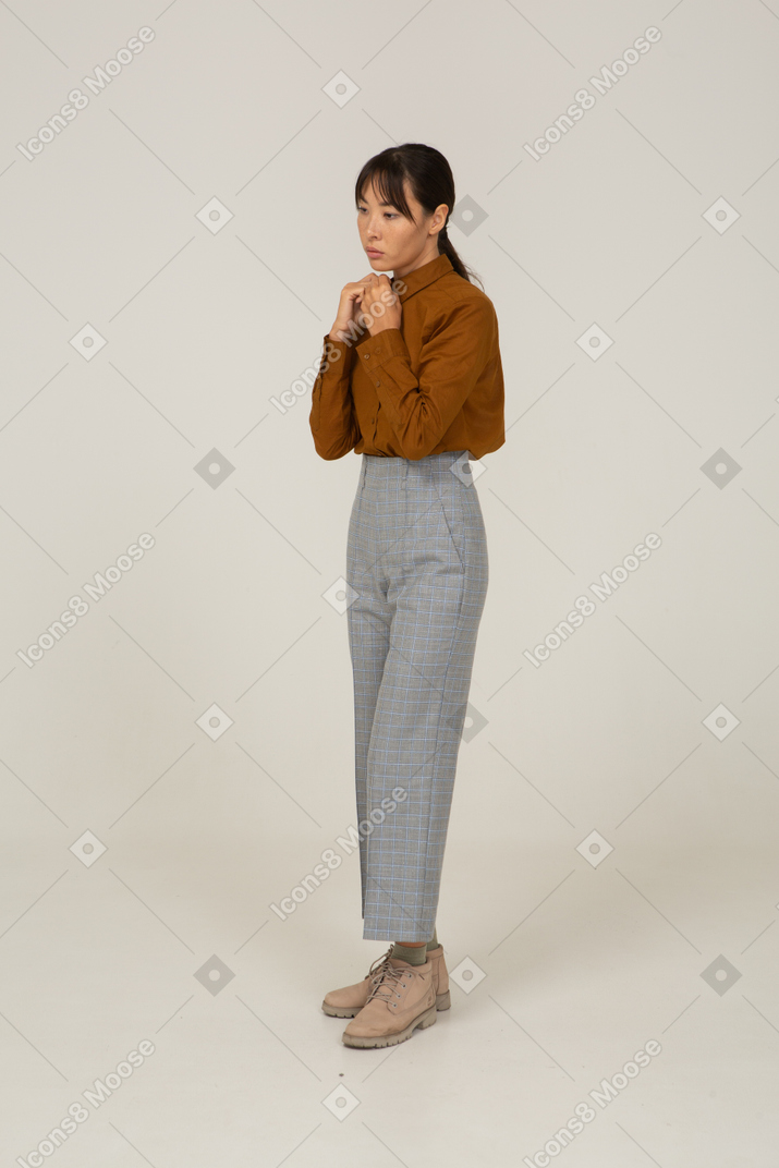 Vista di tre quarti di una giovane donna asiatica in calzoni e camicetta che si tiene per mano insieme