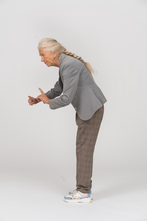 Vista lateral de uma senhora idosa de terno se curvando e mostrando um sinal de alerta