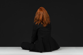 A back side view of the cute red haired woman sitting on the white table