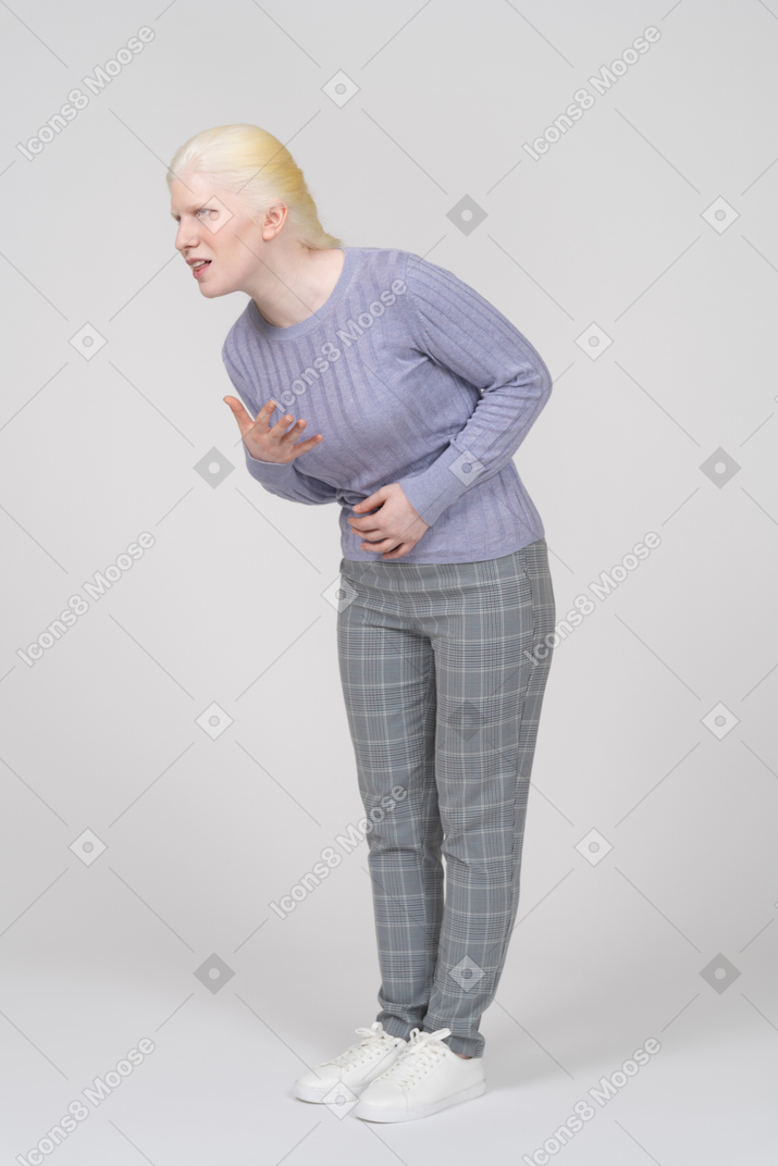 Mujer joven agachándose y gimiendo con dolor de estómago