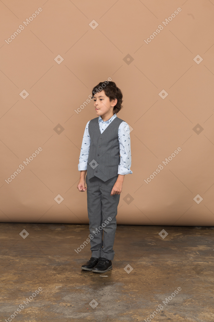 Front view of a cute boy in grey suit standing still and looking aside