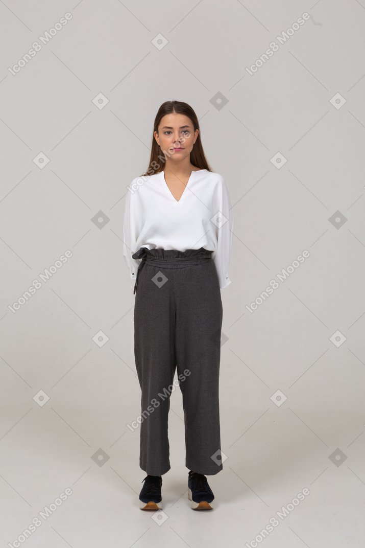 Front view of a young lady in office clothing looking aside and holding hands behind