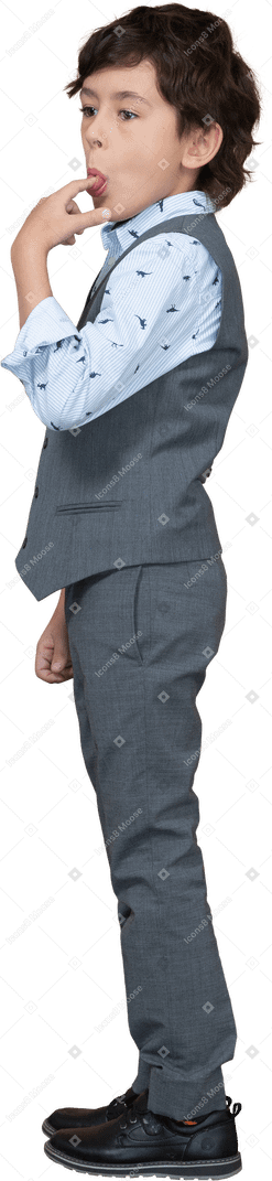 Vista laterale di un ragazzo in abito grigio che si lecca il dito