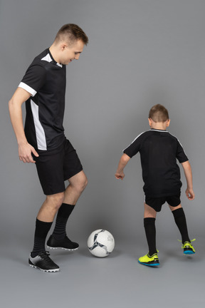 De cuerpo entero de un joven entrenando a un niño pequeño cómo jugar fooyball