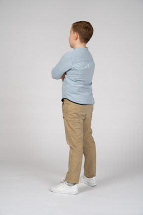 Vista lateral de um menino fofo em pé com os braços cruzados