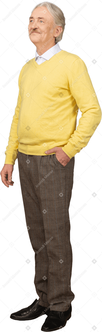 Dreiviertelansicht eines erfreuten alten mannes in einem gelben pullover, der hand in tasche steckt und beiseite schaut
