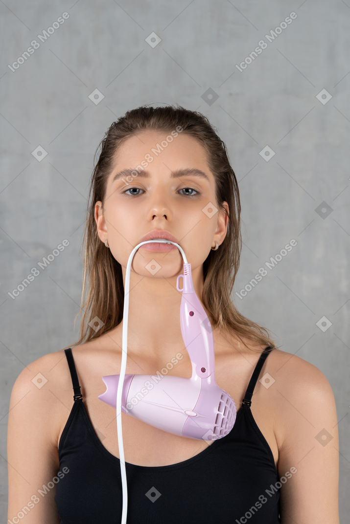 Front view of a beautiful young woman holding hairdryer cord in her teeth