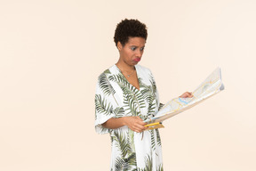 Black short-haired woman in a white and green dress, standing with an international passport and a map in her hands