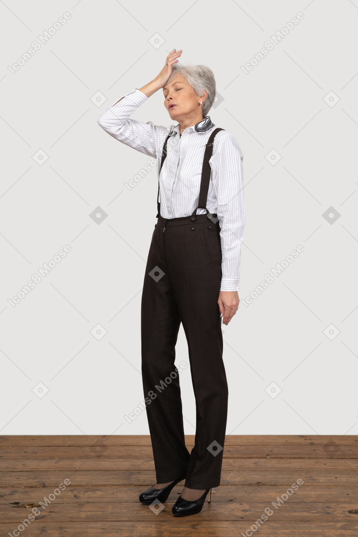 Three-quarter view of an old lady in office clothing touching her forehead