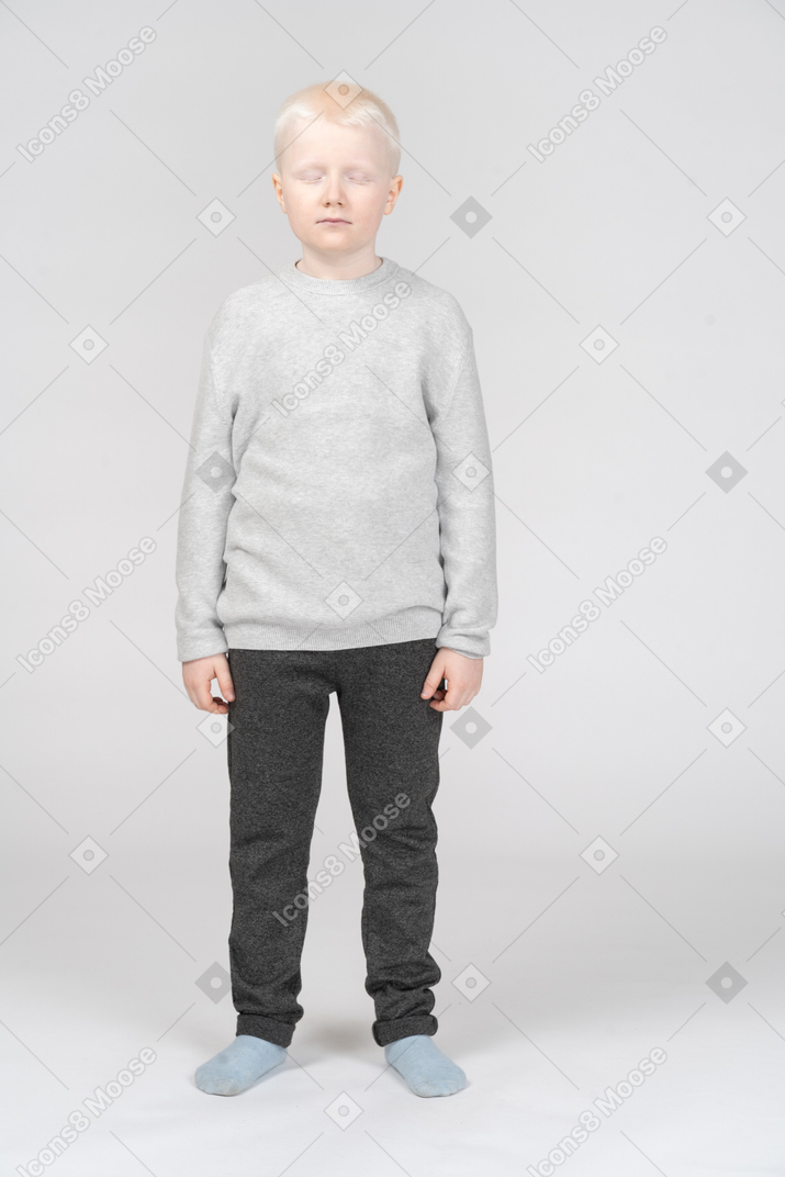 Full-length of a kid blonde boy standing still with his closed