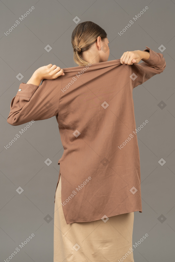 一个女人用两只手脱掉衬衫的后视图