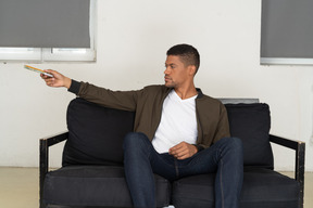 Front view of young man sitting on a sofa and passing pensil with notebook