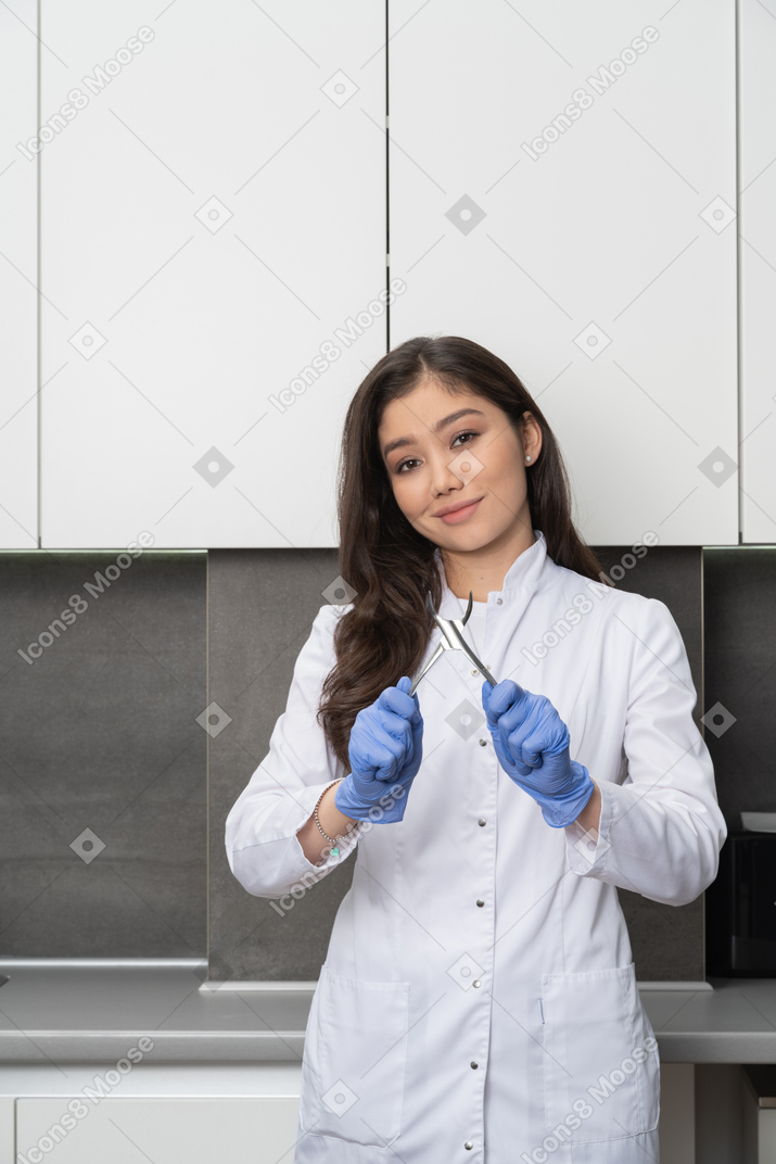 Front view of a smiling female doctor looking at camera and holding dental instrument