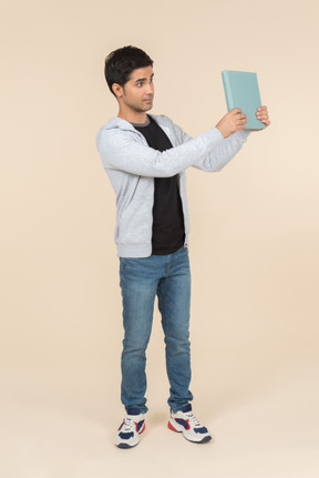 Young caucasian man pointing at book he's holding