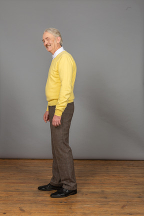 그의 눈을 가진 노란색 스웨터를 입고 웃는 노인의 측면보기 폐쇄