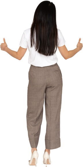 Vista traseira de uma jovem sorridente de calça e camiseta mostrando os polegares para cima