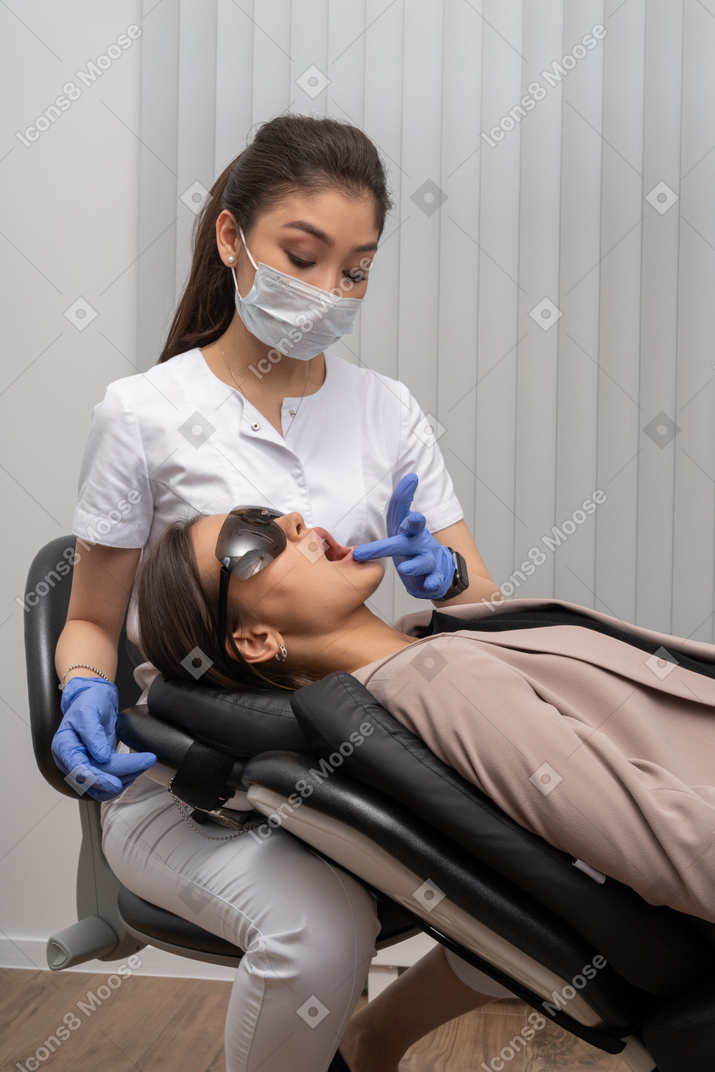 A female dentist in mask examining her patient in medical glasses