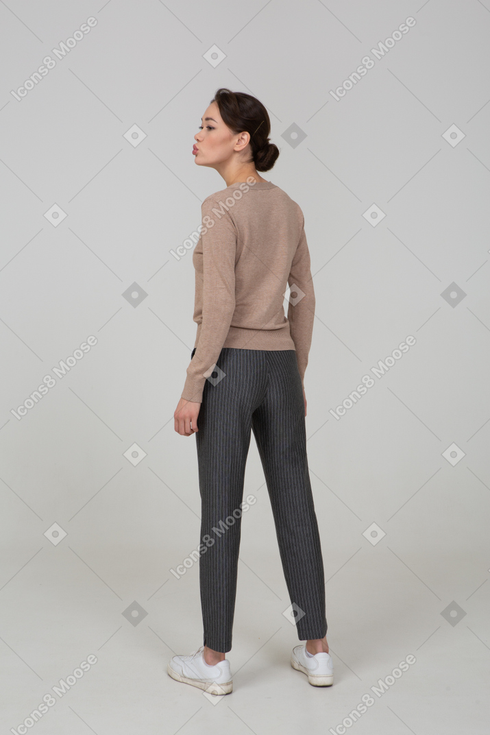 Three-quarter back view of a pouting young lady in pullover and pants