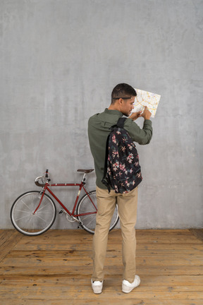 Back view of a man with a backpack and a map asking for directions