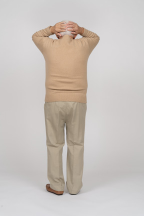 一位身穿休闲服、双手放在头上站立的老人的后视图