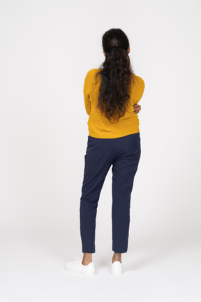 Vista posteriore di una ragazza in abiti casual in piedi con le braccia incrociate