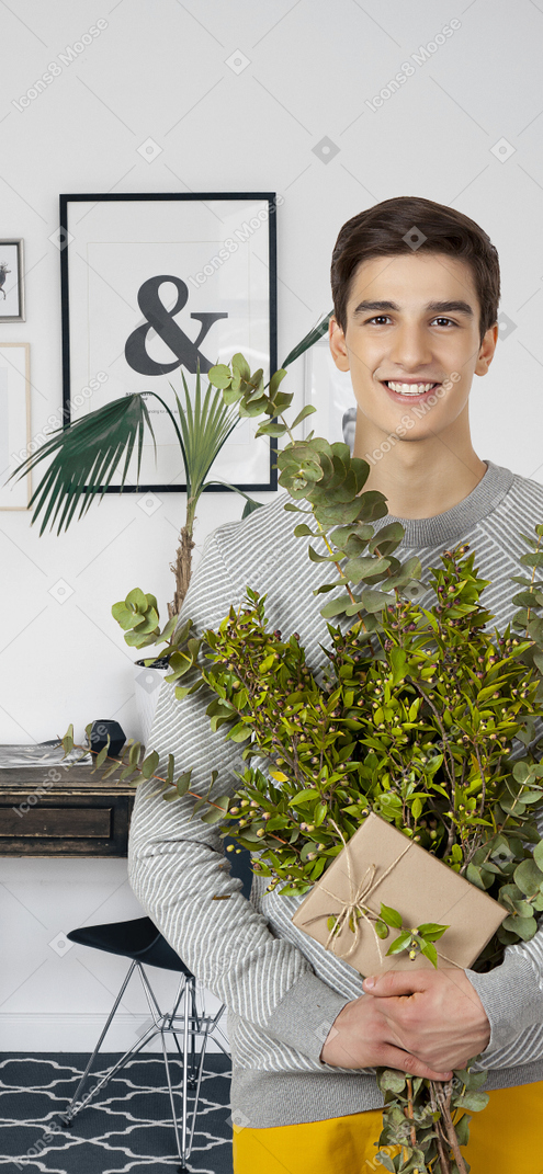 Apuesto hombre sonriente sosteniendo ramas verdes y presente