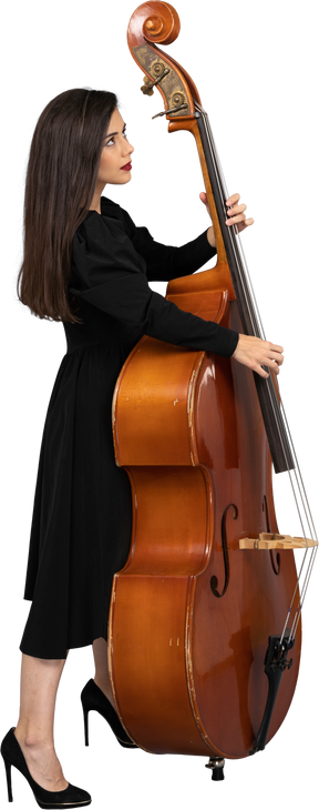 Vista laterale di un serio giovane musicista femminile in abito nero che suona il suo contrabbasso