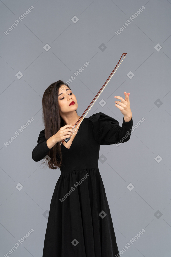 Вид спереди молодой дамы в черном платье, производящей впечатление игры на скрипке