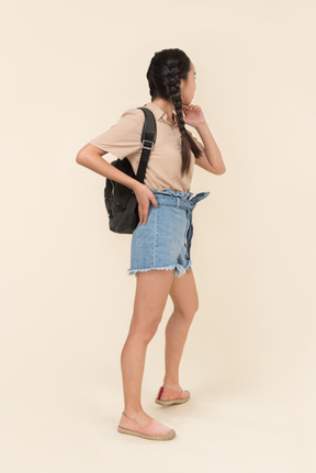 Вид сзади на стоящую молодую женщину с рюкзаком