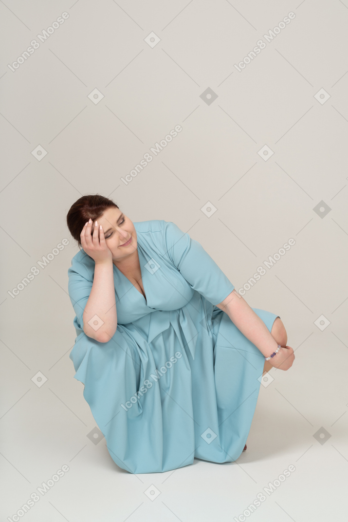 Женщина в синем платье сидит на корточках, вид спереди