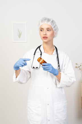 Вид спереди молодой женщины-врача, указывая пальцем на банку с таблетками