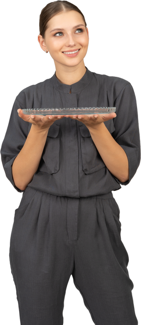Front view of a young woman in a jumpsuit holding glass plate