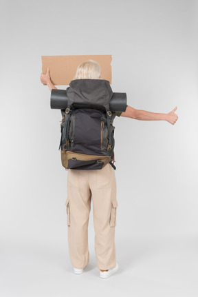 Female tourist hitchhiker carrying backpack and standing back to camera