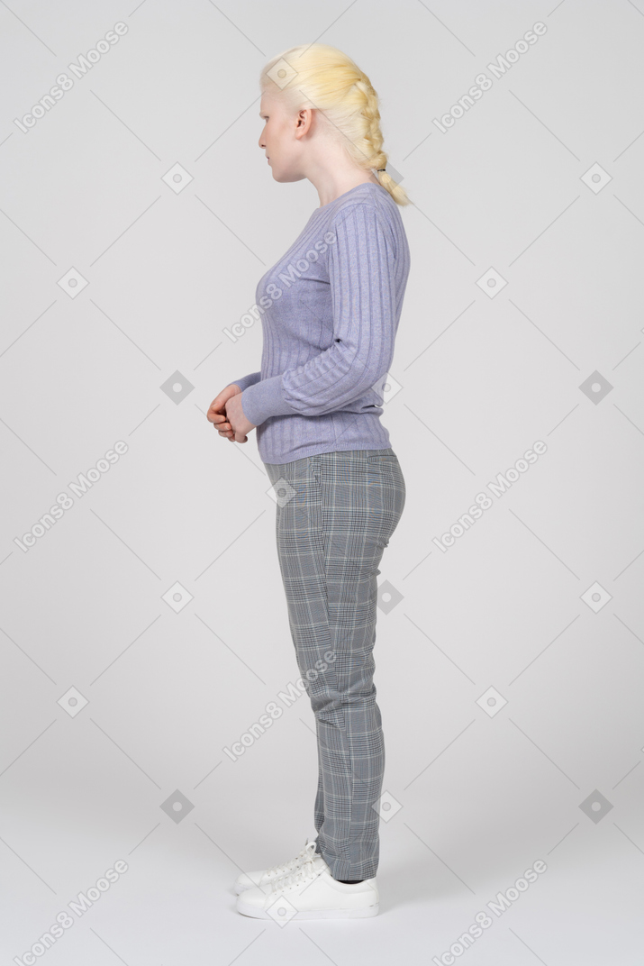 Side view of a blonde woman standing with her hands folded and looking aside