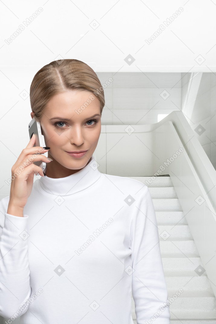 A woman talking on a cell phone while standing in front of a staircase