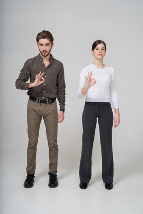 Vista frontale di una giovane coppia in abiti da ufficio che mostra segno ok