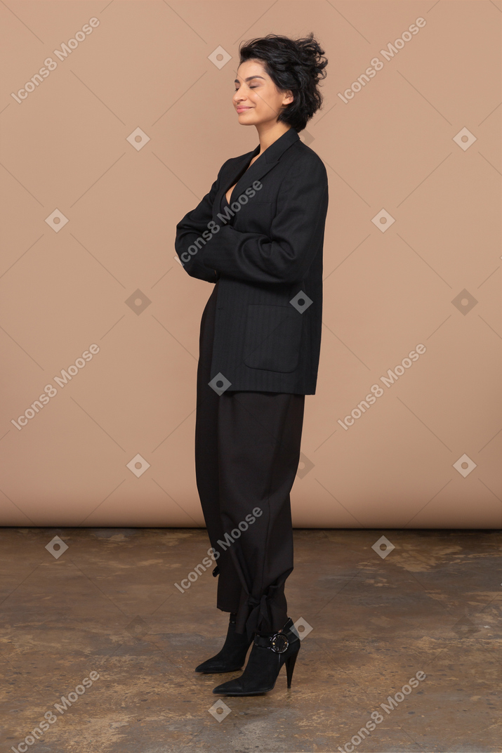 Вид в три четверти на бизнесвумен в черном костюме, обнимающую себя с закрытыми глазами