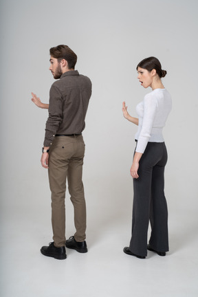 Vista posterior de tres cuartos de una pareja joven en ropa de oficina extendiendo la mano