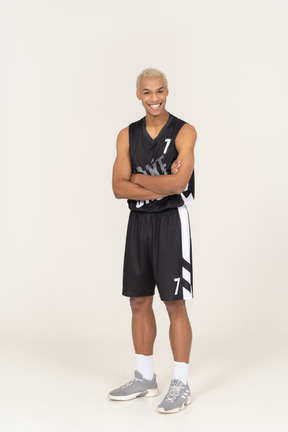 Vista di un giovane giocatore di basket maschio sorridente che incrocia le braccia