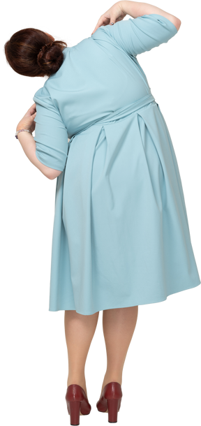 Rear view of a woman in blue dress posing with hands on shoulders