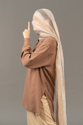 Side view of a woman covered with scarf showing a silence gesture