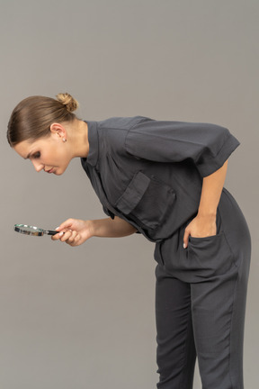 Three-quarter view of a young woman in a jumpsuit holding a magnifying glass