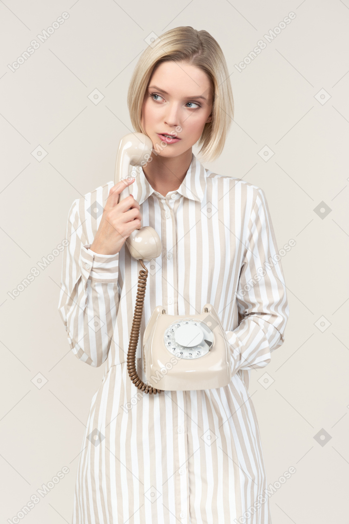Pensive young woman holding old rotary phone