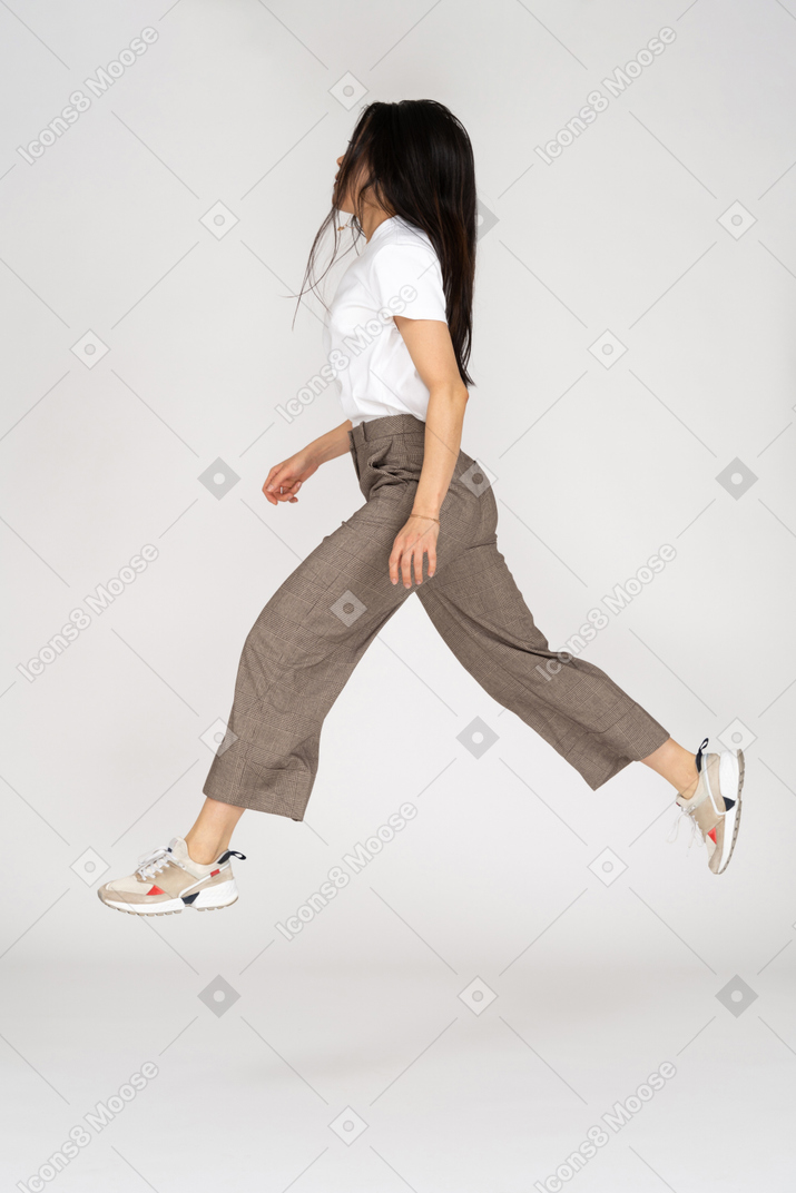 Vista laterale di una giovane donna che salta in calzoni e t-shirt gambe distese