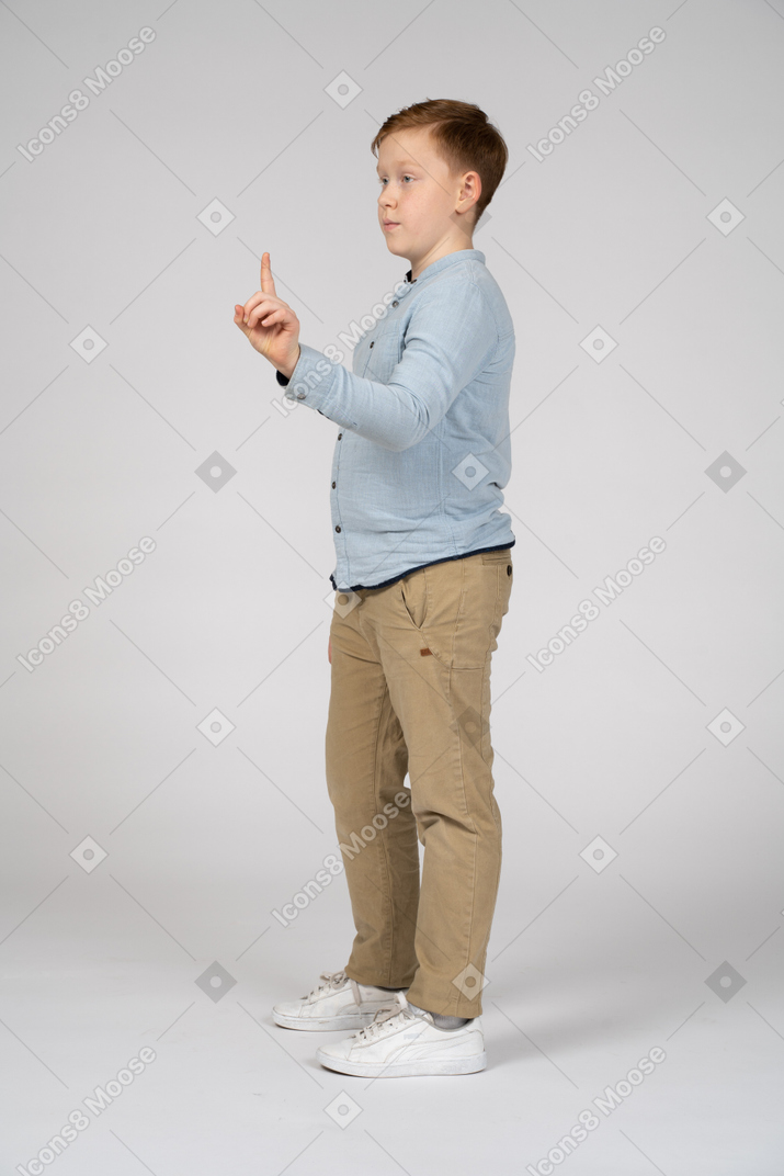 Vista lateral de um menino apontando para cima com o dedo