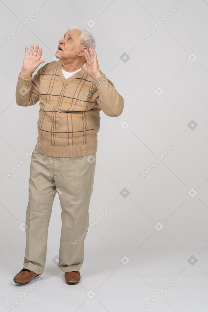 Front view of a scared old man standing with raised arms