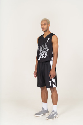 Three-quarter view of a young male basketball player standing still & looking at camera
