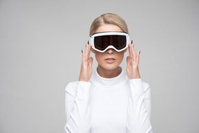 Young blonde woman in white turtleneck adjusting ski goggles