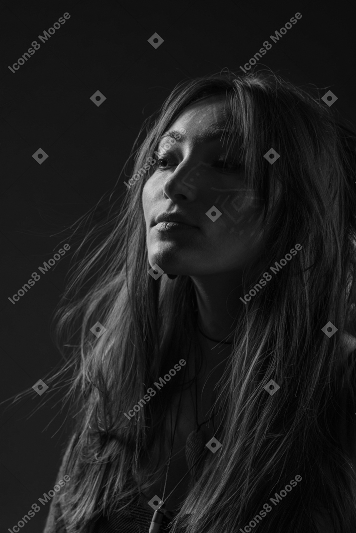 Noir three-quarter portrait of a young female with ethnic facial art and messy hair raising head
