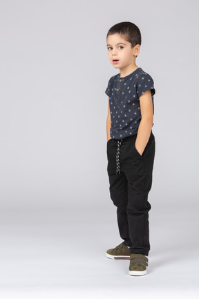 Vista frontal de un niño impresionado posando con las manos en los bolsillos y mirando a la cámara